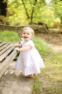 A child in white dress standing beside a wooden bench