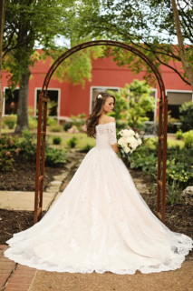 A bride standing in front of a gate holding white flowers