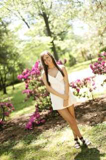 A girl wearing white standing with flowers behind
