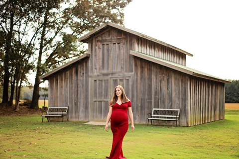 A pregnant woman in red dress in front of a barn