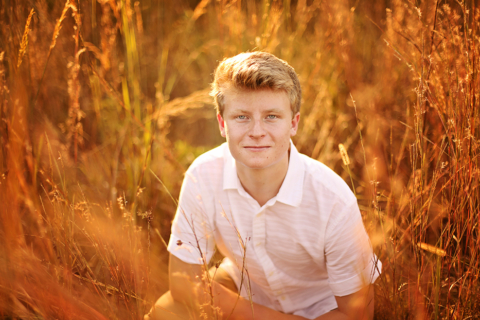 A boy wearing white, sitting with tall grasses