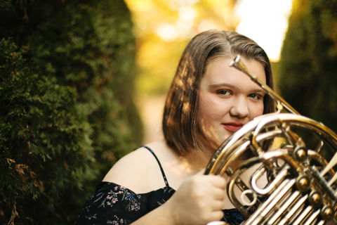 A young woman holding a French horn