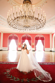 A bride standing in a red theme room with a giant chandelier