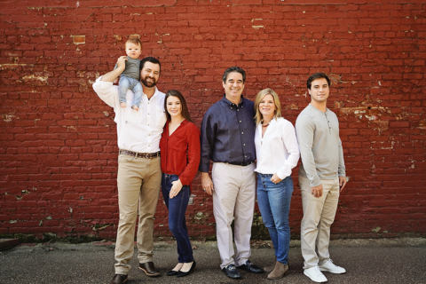 A family of six posing in front of a red wall