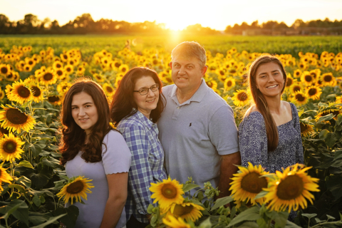 A family of four standing with sunflowers around