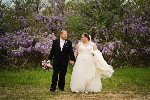 A bride and groom holding hands in front of purple flowers