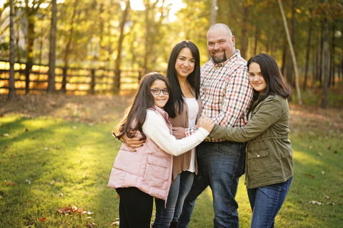 A family of four holding each other standing on grass