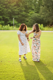 two girls standing on grass with trees in background