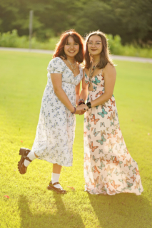 two women standing on grass with trees in background