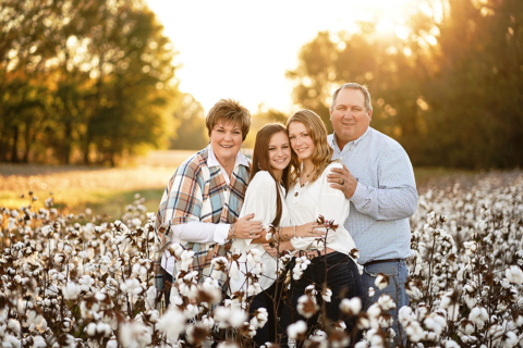 A family of four standing with cotton plants surrounding