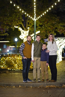 A family of four standing together with lights behind
