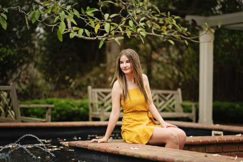 A girl wearing yellow dress sitting on a brick wall
