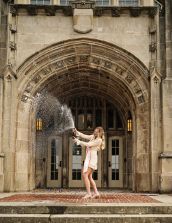 A woman spraying champagne in front of a big gate