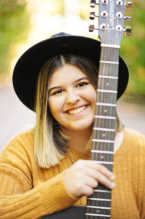 A girl wearing a hat holding a guitar in hand