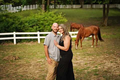 A man and a woman standing with horses in the background