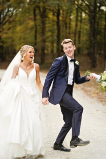 A bride and groom dancing on the road in front of a forest