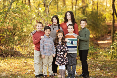 A family of seven standing with trees behind them