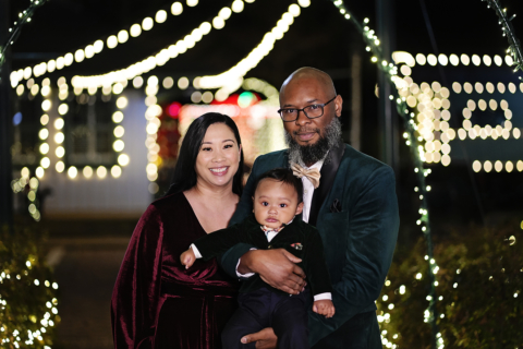 A family of three in front of Christmas lights