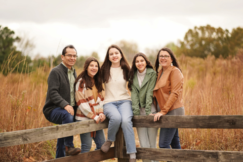 A family of five posing on a wooden fence