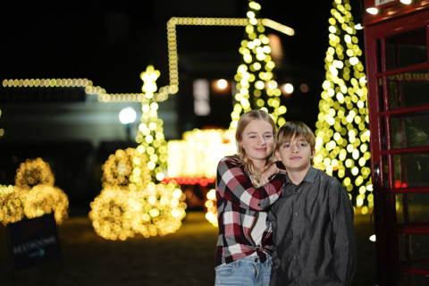 A girl and boy standing in front of Christmas lights.