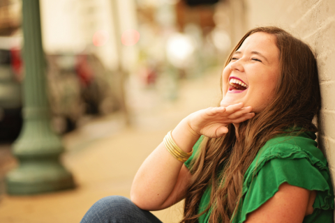 A girl wearing green laughing in front of a wall
