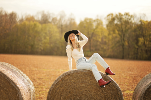 A woman is sitting on hay bales in a field