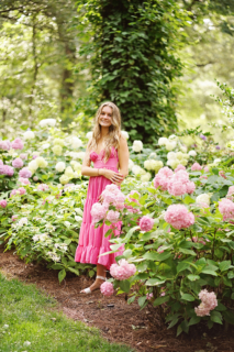 A girl wearing pink dress and standing beside flower plants
