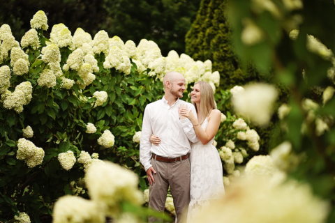 man and a woman standing together in front of white flowers