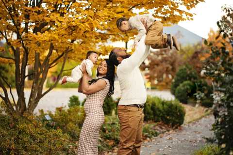 A couple holding their two children in front of trees