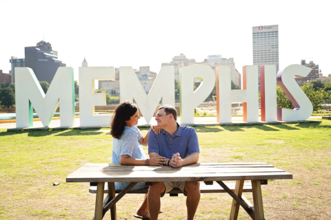 A man and a woman siting on a bench with Memphis behind