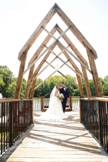 A bride and groom standing on a wooden bridge