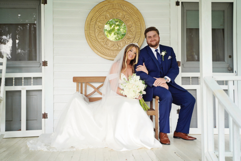 A bride and groom siting on a bench beside front door